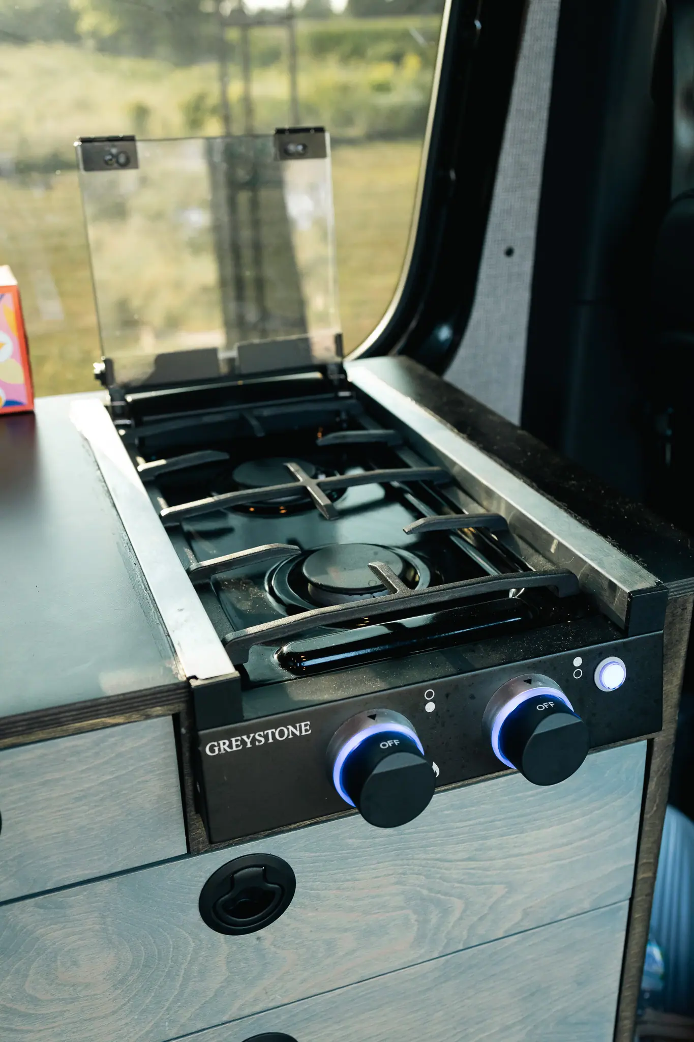 Two-burner gas cooktop with a glass lid built into the galley of a Sprinter camper van