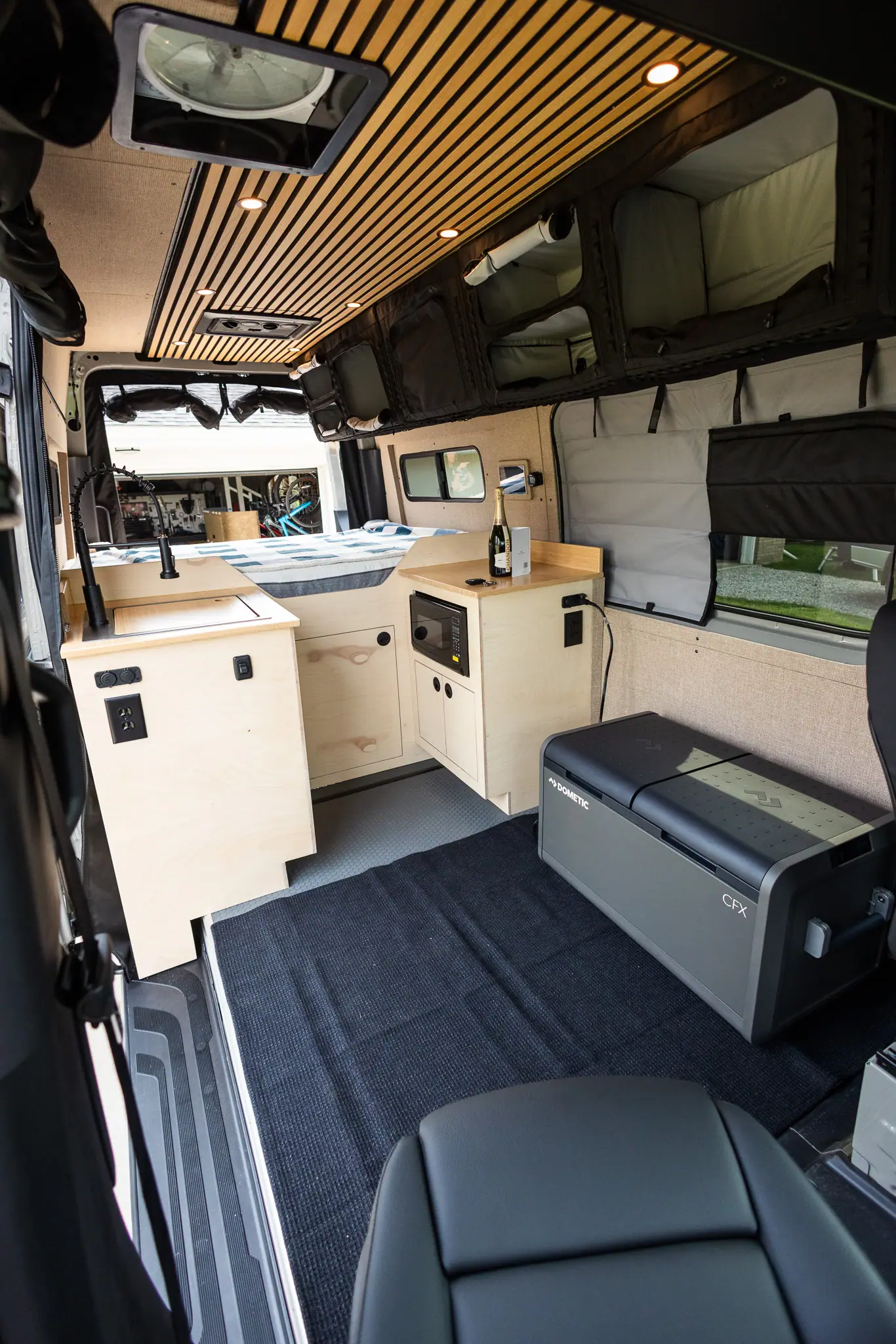 Sprinter camper van interior with birch cabinets, a galley, fridge, wood slat ceiling and rear bed