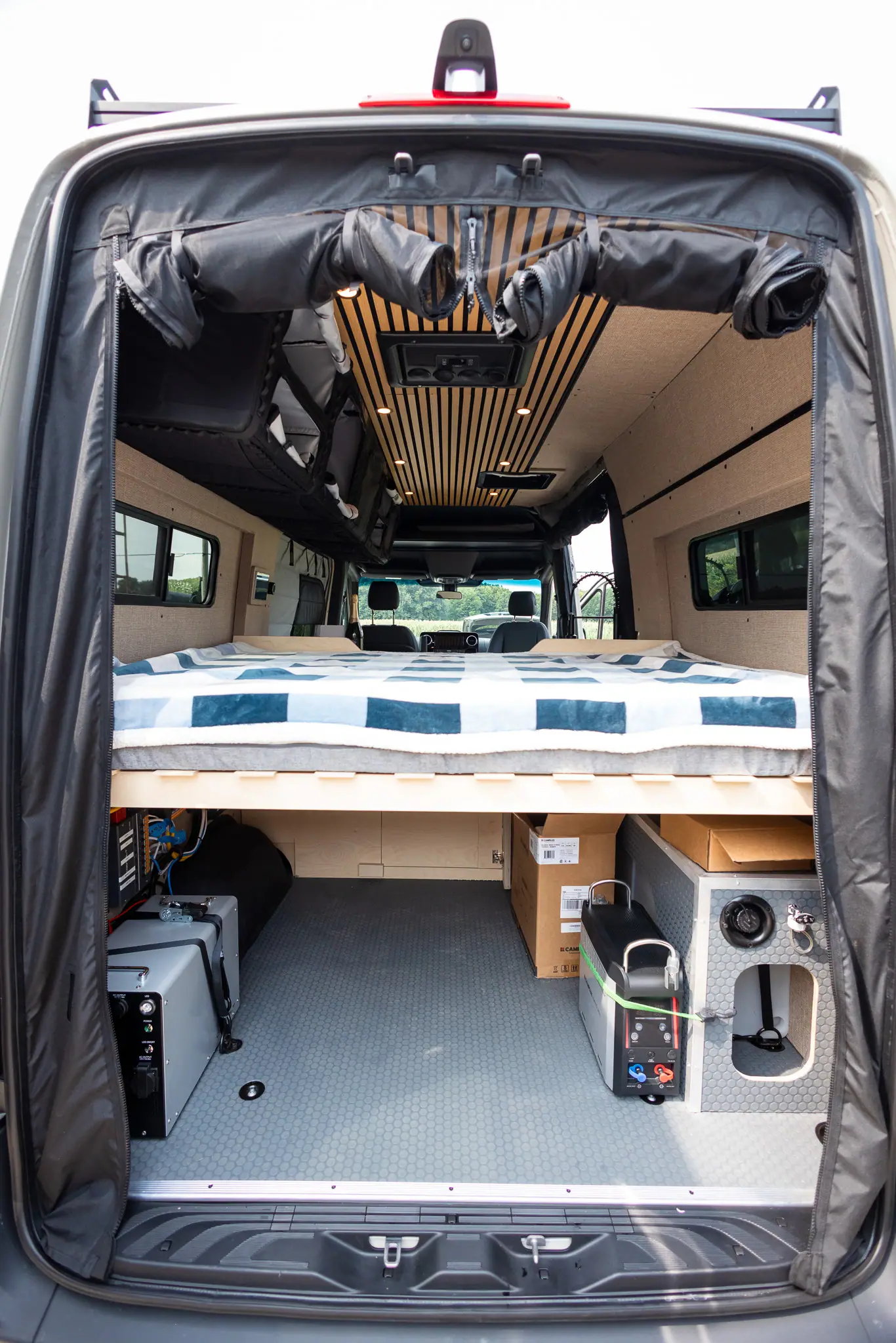 Looking through the rear doors of a Sprinter camper van at the bed, the storage garage below and the slat ceiling