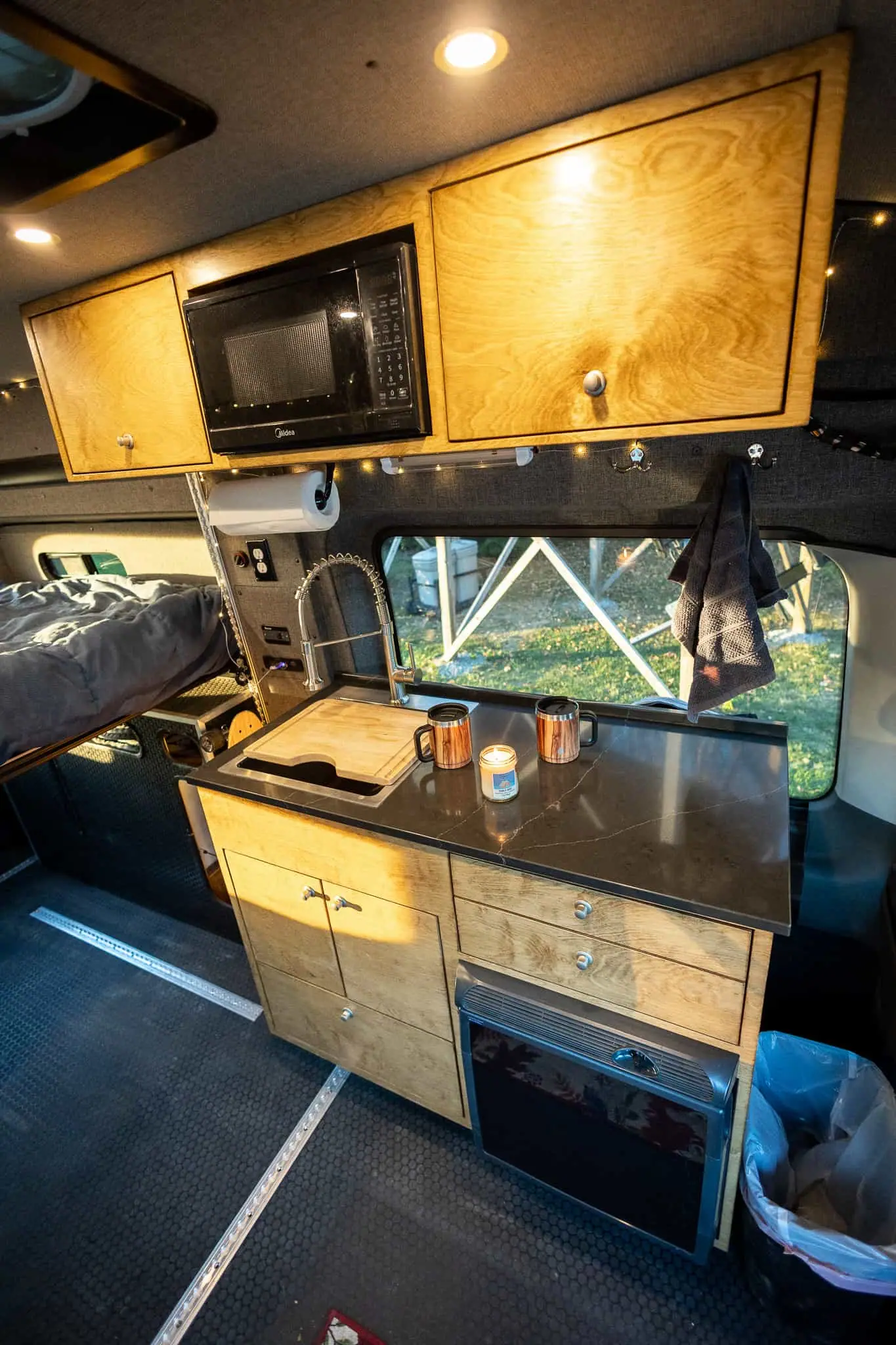 Ford Transit camper van galley with stained cabinets, microwave, black countertop, sink and built-in fridge