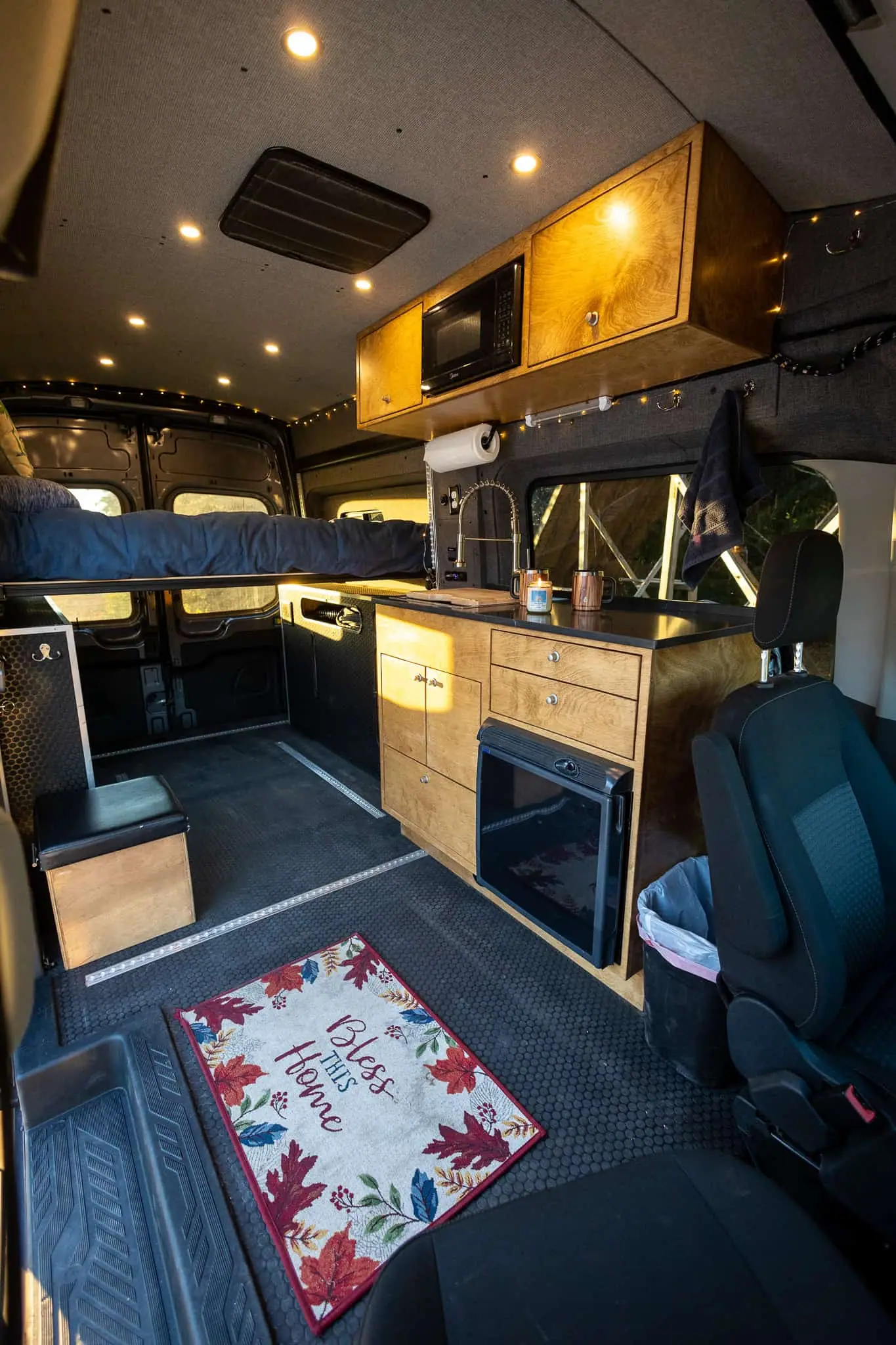 Ford Transit camper van interior with stained galley cabinets, microwave, sink, fridge and a rear platform bed