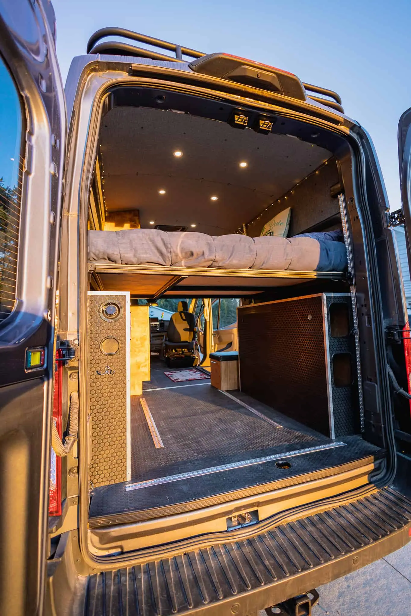 Rear doors open on a Ford Transit camper van, showing the platform bed and under-bed gear garage